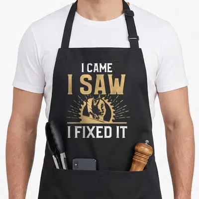 Joke carpentry apron - Distressed white and tan text I CAME I SAW I FIXED IT around carpenter and circular saw graphic — shown on a black cotton canvas apron against a white background