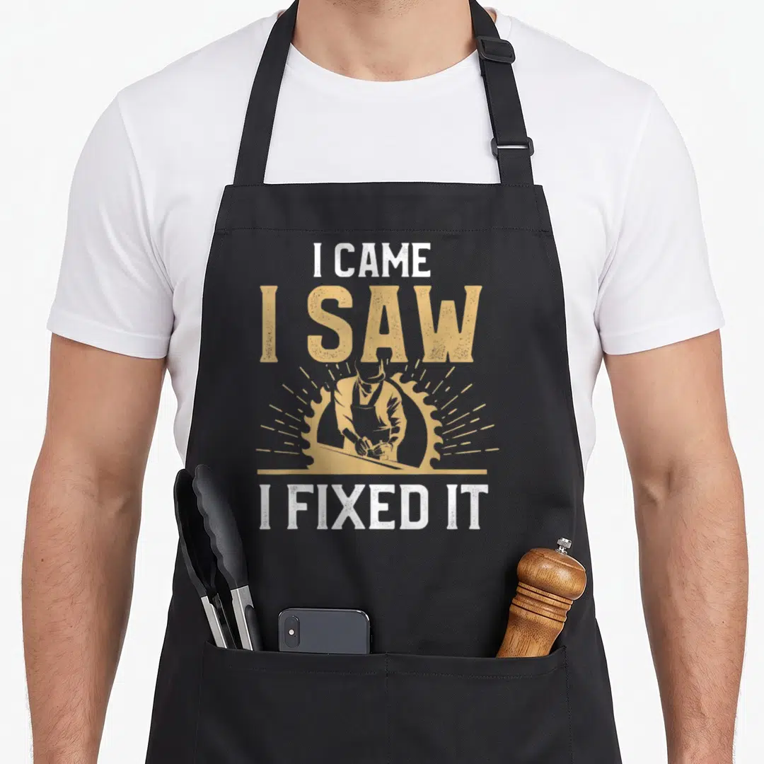 Joke carpentry apron - Distressed white and tan text I CAME I SAW I FIXED IT around carpenter and circular saw graphic — shown on a black cotton canvas apron against a white background