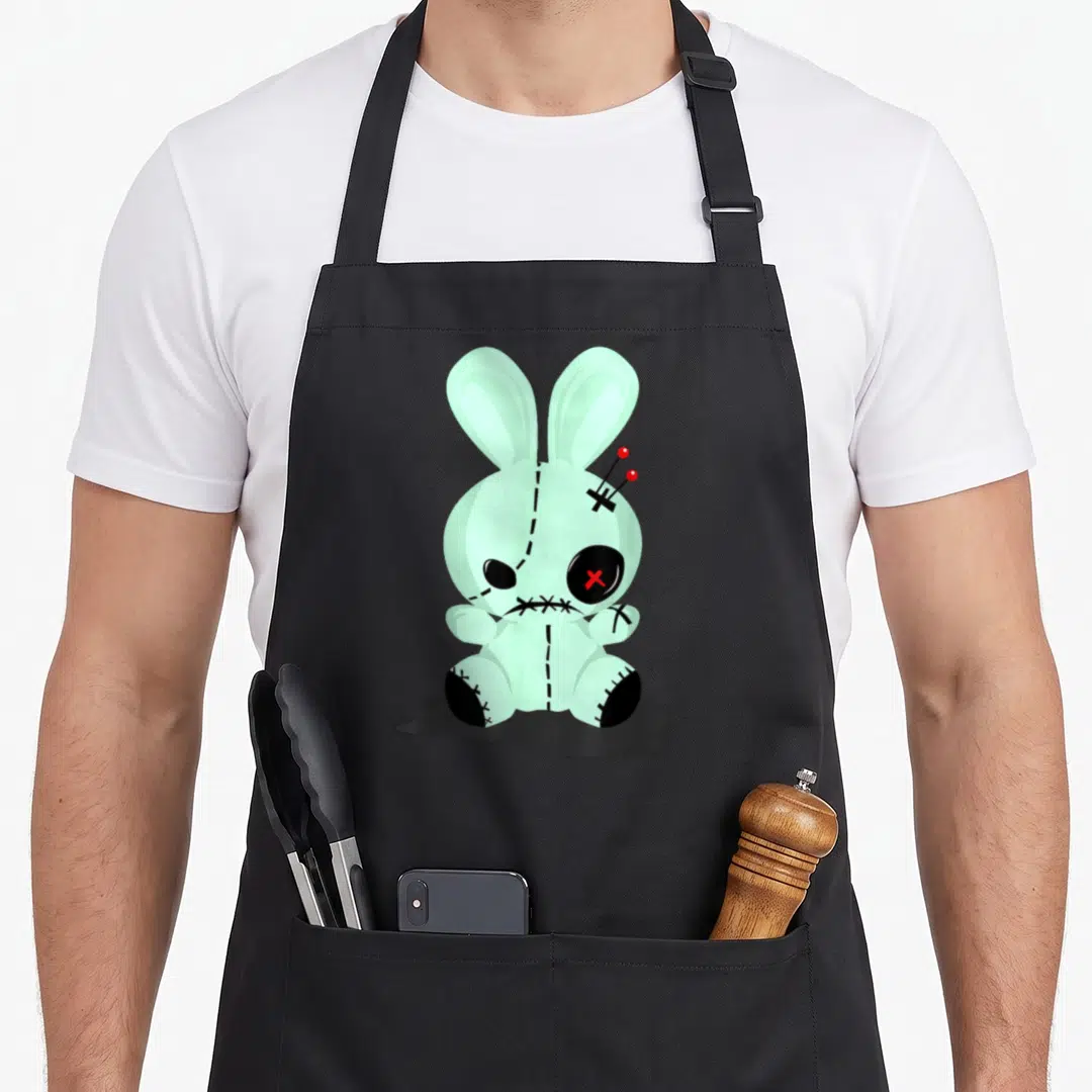 Voodoo goth apron - Mint green stitched bunny with red pins and black X eye on dark shadow — shown on a black cotton canvas apron against a white background