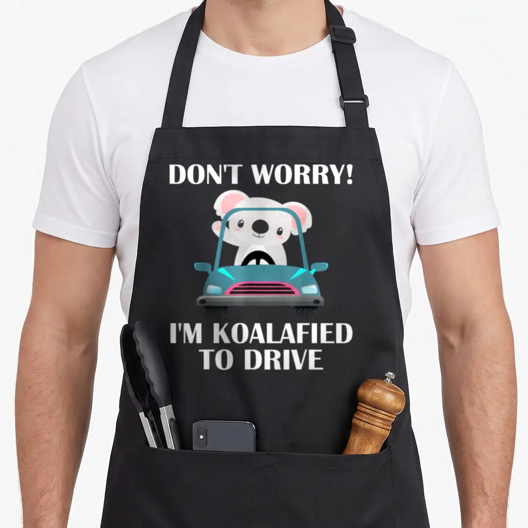 Koalafied funny worry apron - Cartoon koala waving from blue car with text DON'T WORRY I'M KOALAFIED TO DRIVE — shown on a black cotton canvas apron against a white background
