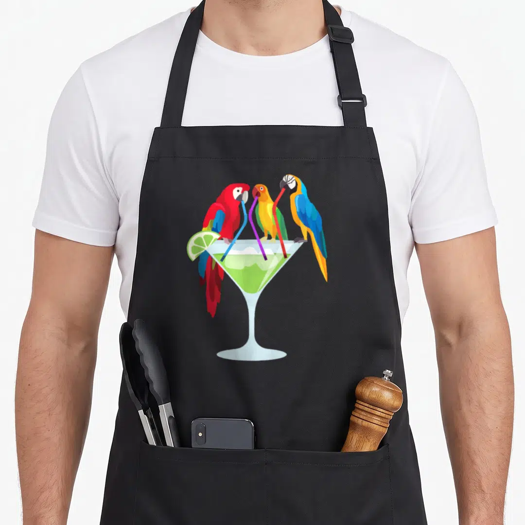 Margarita hawaiian apron - Three cartoon parrots in red yellow blue green drinking via straws from a martini glass — shown on a black cotton canvas apron against a white background