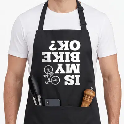 Upside bicycle apron - Upside down text IS MY BIKE OK? next to a small white bicycle illustration — shown on a black cotton canvas apron against a white background