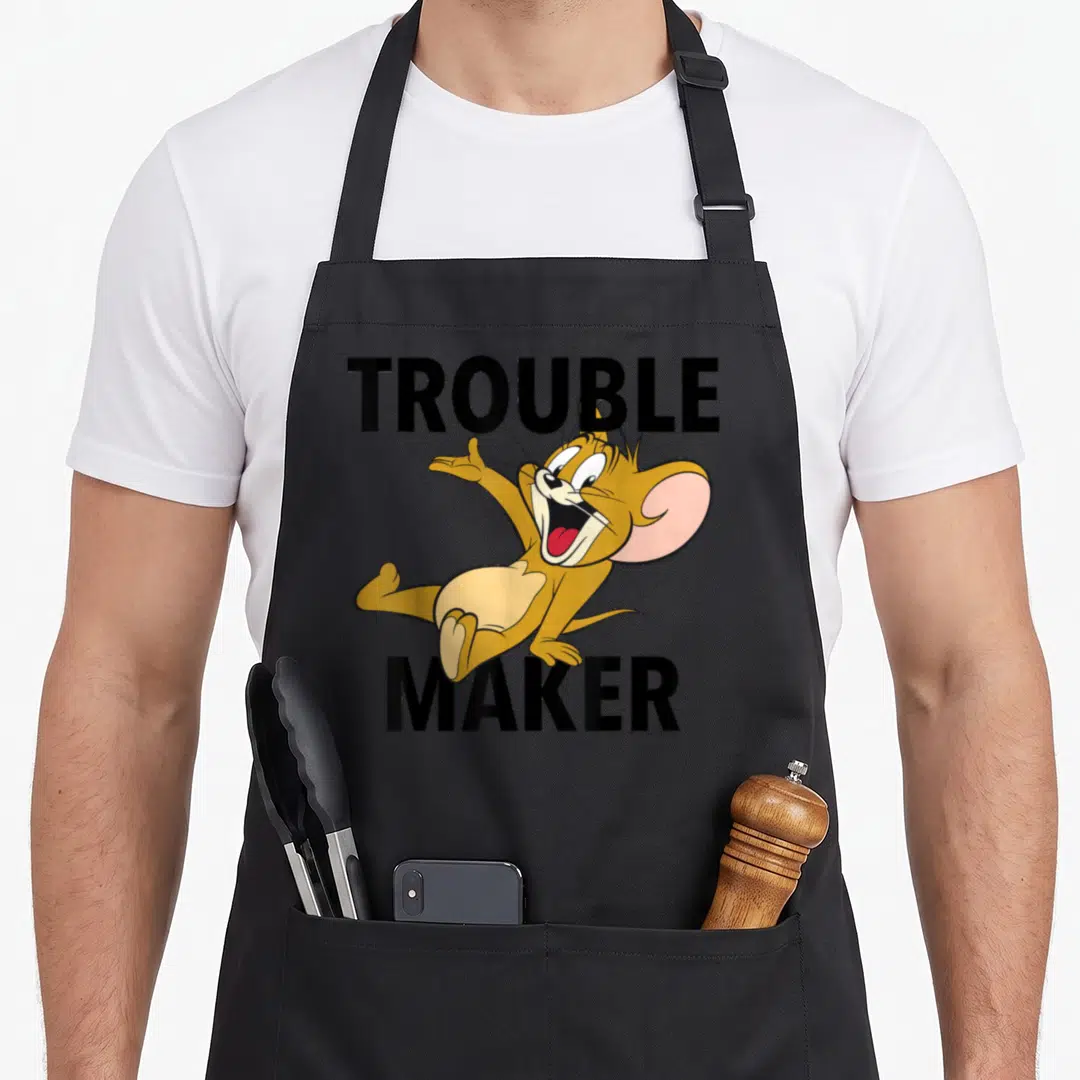 Trouble maker apron - Cartoon mouse leaping between bold TROUBLE MAKER text in black and yellow-brown — shown on a black cotton canvas apron against a white background