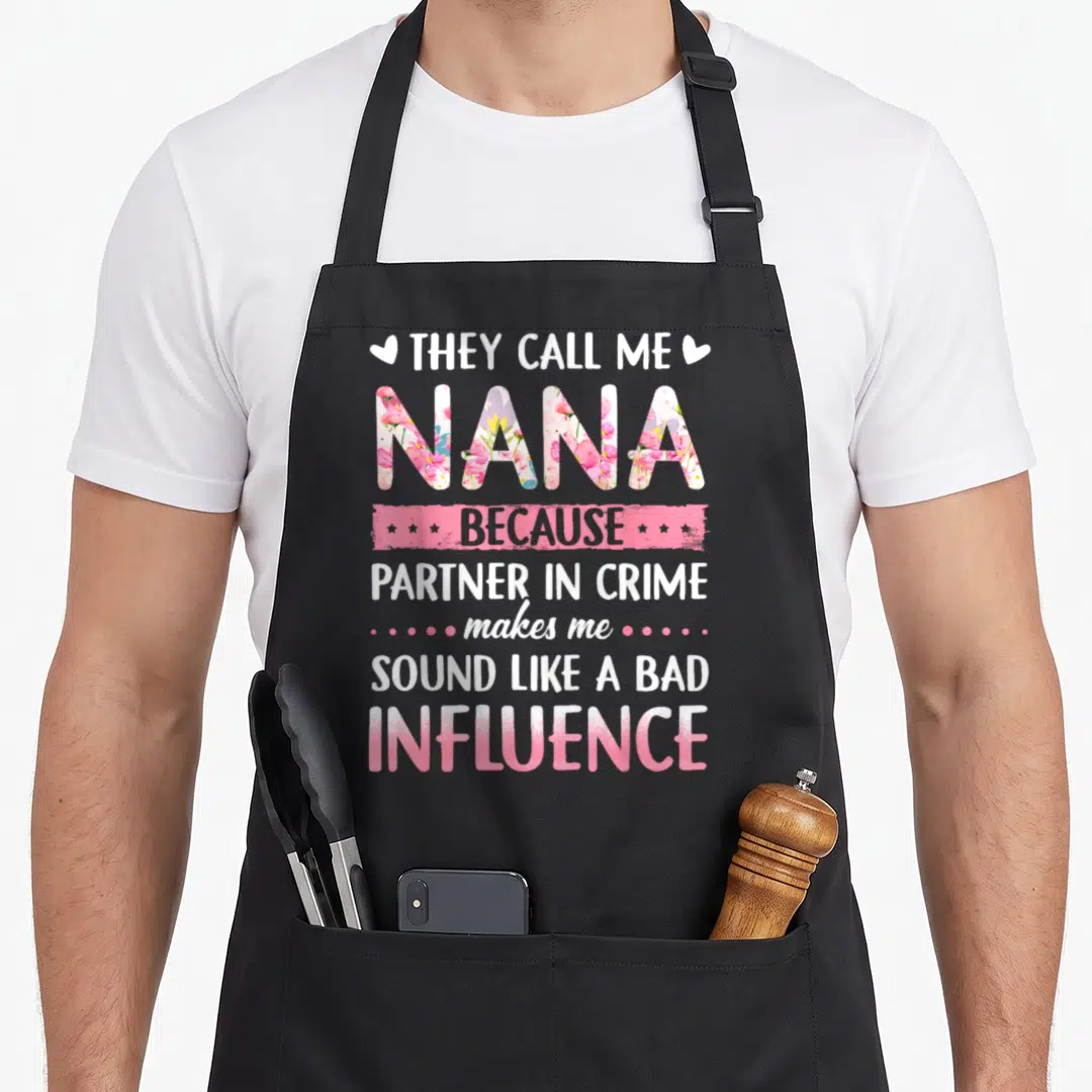 They nana aprons - Stacked text quote with floral NANA letters and pink banner — shown on a black cotton canvas apron against a white background