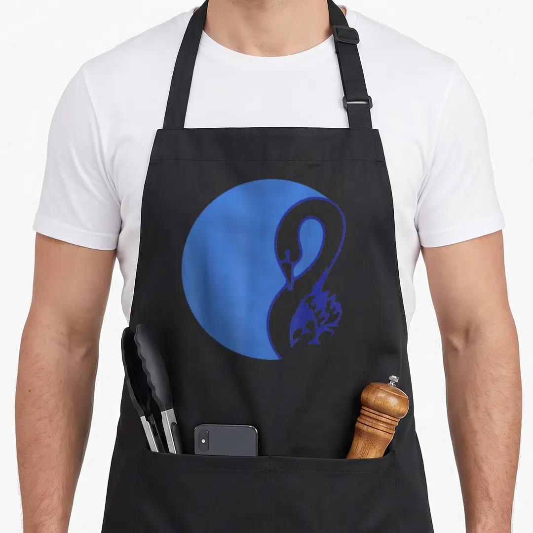 General bird apron - Minimalist dark blue swan outline overlapping a solid blue circle on black fabric — shown on a black cotton canvas apron against a white background