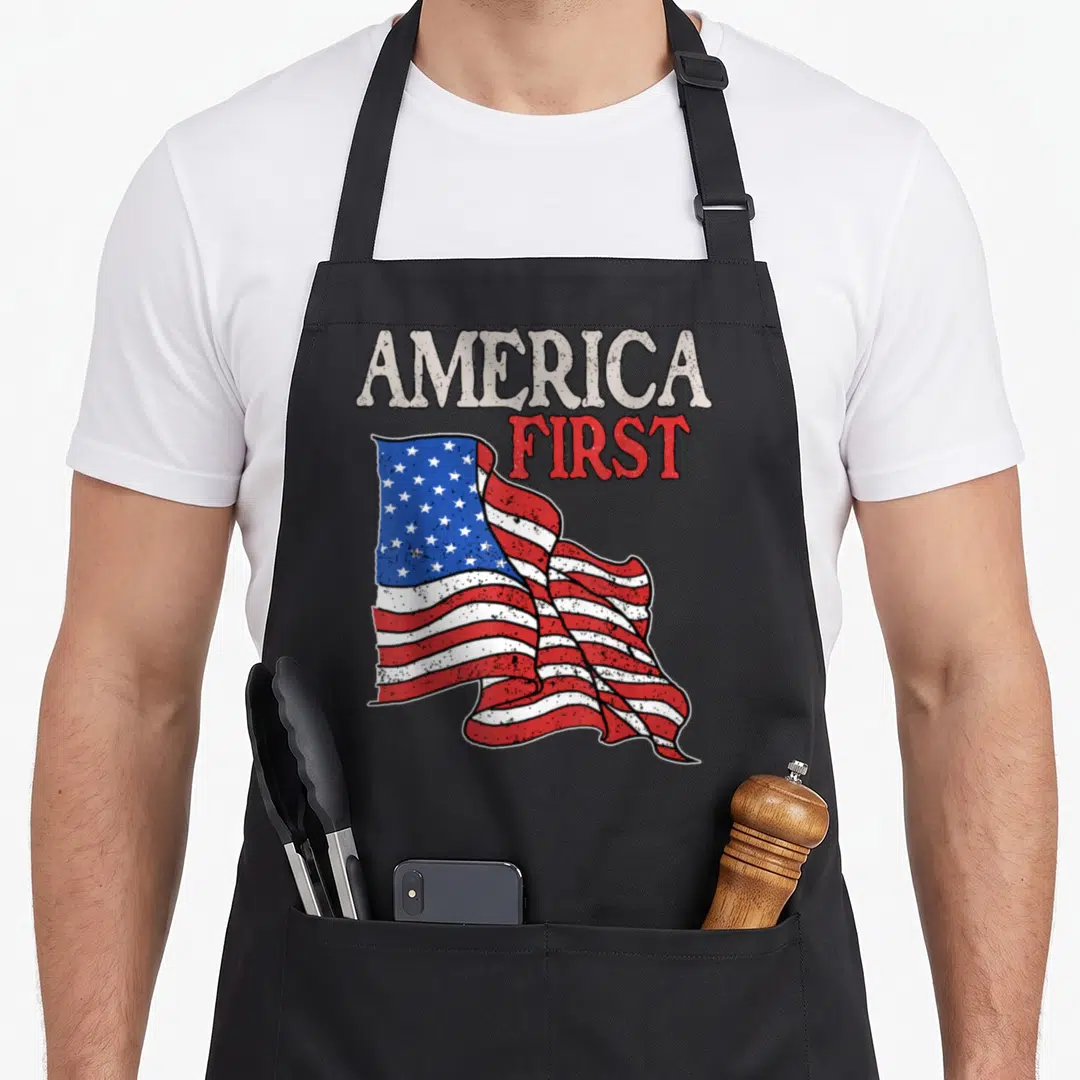 Patriot memorial american flag apron - Waving USA flag with distressed AMERICA FIRST text in red white and blue — shown on a black cotton canvas apron against a white background