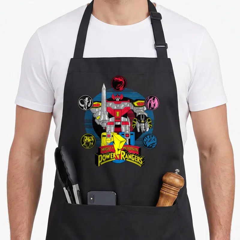 Megazord rangers apron - Red and silver robot surrounded by five colored dinosaur head icons and logo text — shown on a black cotton canvas apron against a white background