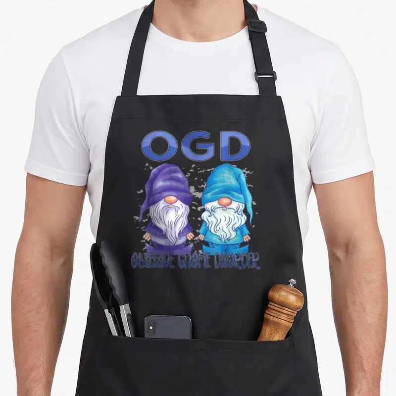Garden gnome apron - Two cartoon gnomes in blue and purple plaid under OGD text — shown on a black cotton canvas apron against a white background