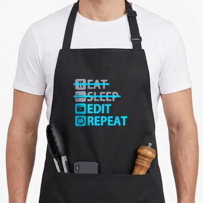 Eat edit apron - Light blue text EAT SLEEP EDIT REPEAT with film icons and strikethroughs — shown on a black cotton canvas apron against a white background