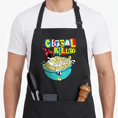 Cereal breakfast apron - CEREAL KILLER ransom note text above red figure and blue bowl of cereal rings — shown on a black cotton canvas apron against a white background