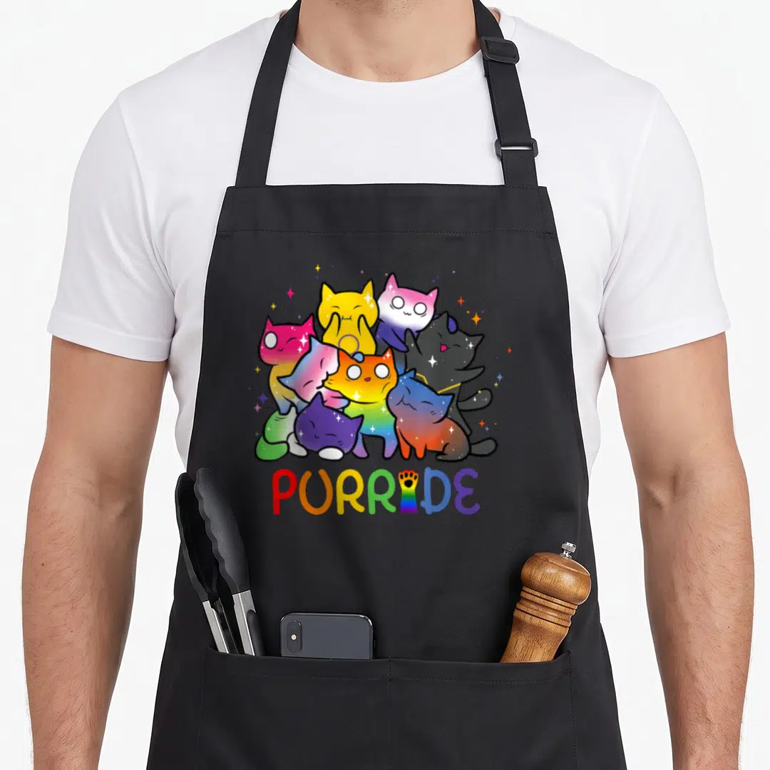 Purride animal apron - Rainbow cats clustered above PURRIDE with paw-print I, cartoon style — shown on a black cotton canvas apron against a white background