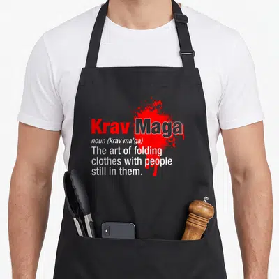 Martial israeli boy apron - Red splatter behind stacked white text defining Krav Maga as folding clothes with people — shown on a black cotton canvas apron against a white background