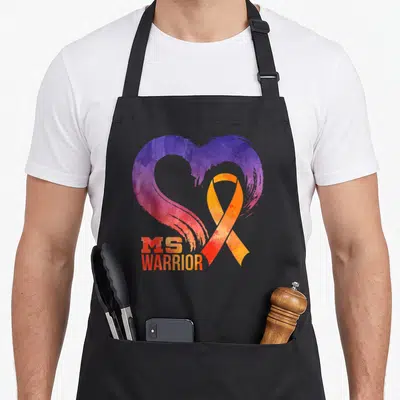 Month multiple sclerosis awareness apron - Watercolor heart in purple and pink with orange ribbon and MS WARRIOR text — shown on a black cotton canvas apron against a white background