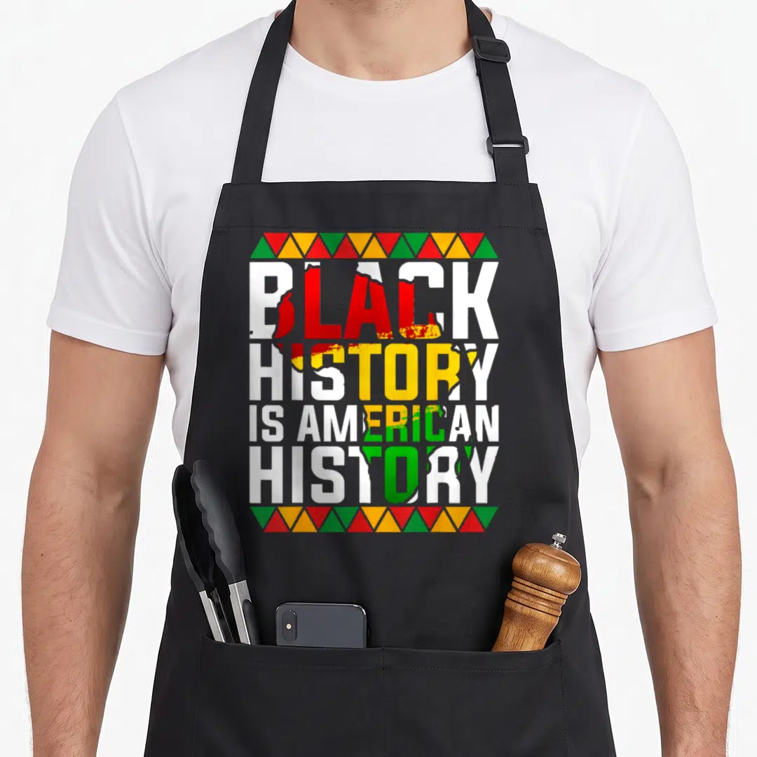 Patriotic african american aprons - Stacked white text reading BLACK HISTORY IS AMERICAN HISTORY with red yellow green — shown on a black cotton canvas apron against a white background