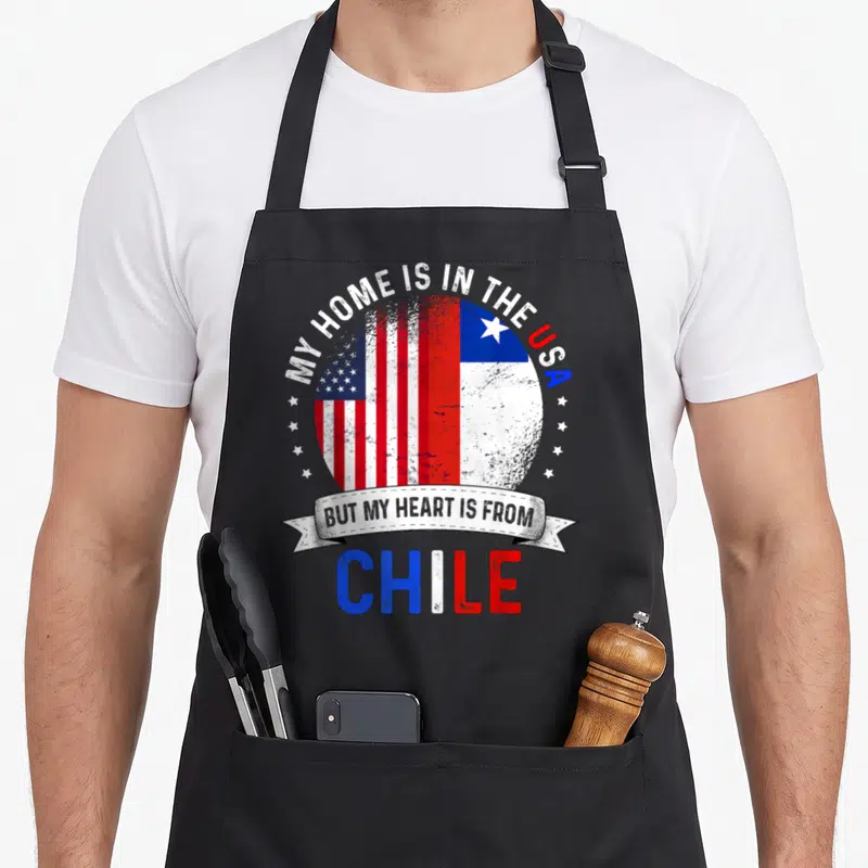 Chile patriots apron - Circular split US and Chile flag with arching text and ribbon reading My Home is in the USA — shown on a black cotton canvas apron against a white background