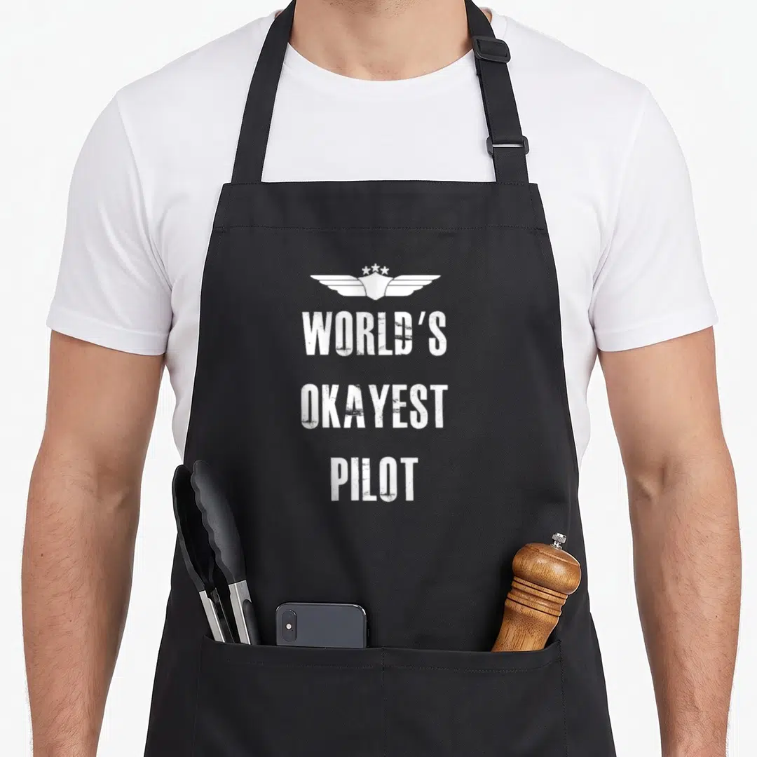 Okayest flying apron - White pilot wings and three lines of distressed text reading okayest pilot on gray background — shown on a black cotton canvas apron against a white background