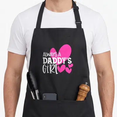 Alway mom daughter aprons - White text ALWAYS A DADDY'S GIRL over large pink heart with three smaller hearts — shown on a black cotton canvas apron against a white background