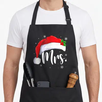 Pajamas mr mrs aprons - Red Santa hat with holly and snowflakes above white Mrs. script text — shown on a black cotton canvas apron against a white background