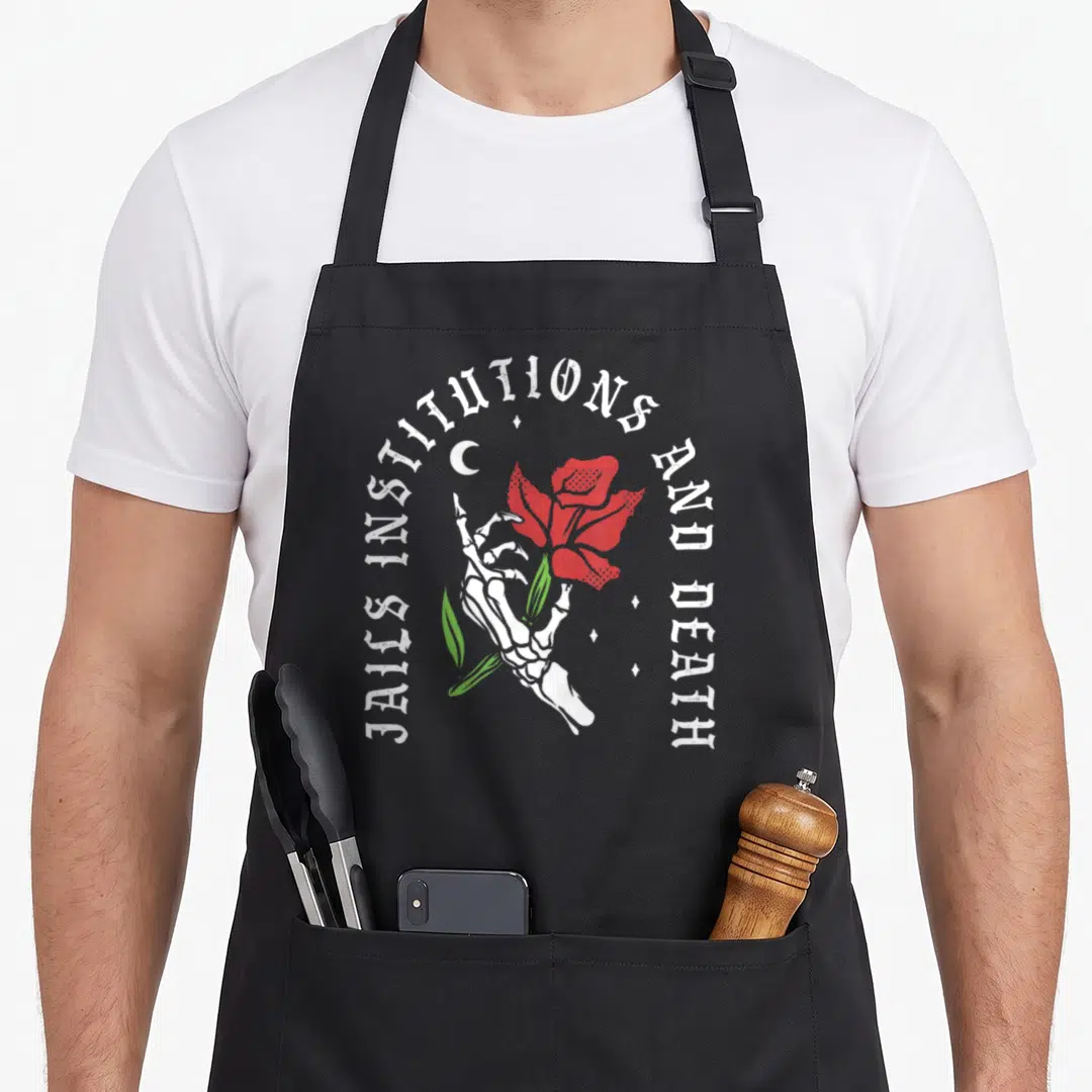Jail sobriety apron - Skeleton hand holding red rose with circular text Jails Institutions and Death — shown on a black cotton canvas apron against a white background