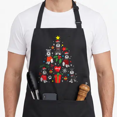 Christmas schnauzer apron - Five cartoon dogs form a Christmas tree with a red heart reading dog, surrounded — shown on a black cotton canvas apron against a white background
