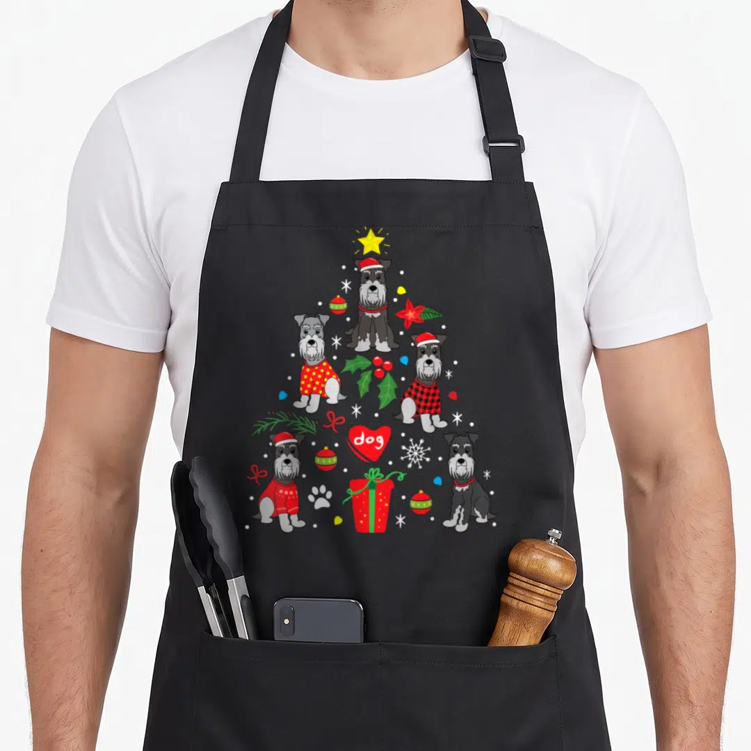 Christmas schnauzer apron - Five cartoon dogs form a Christmas tree with a red heart reading dog, surrounded — shown on a black cotton canvas apron against a white background