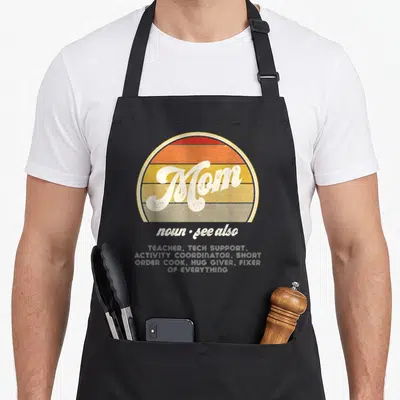 Thank mother's apron - Retro Mom noun text inside red orange yellow tan striped semi-circle with stacked white role — shown on a black cotton canvas apron against a white background