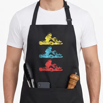 Cart racing apron - Three stacked distressed ATV rider silhouettes in yellow blue red no text — shown on a black cotton canvas apron against a white background
