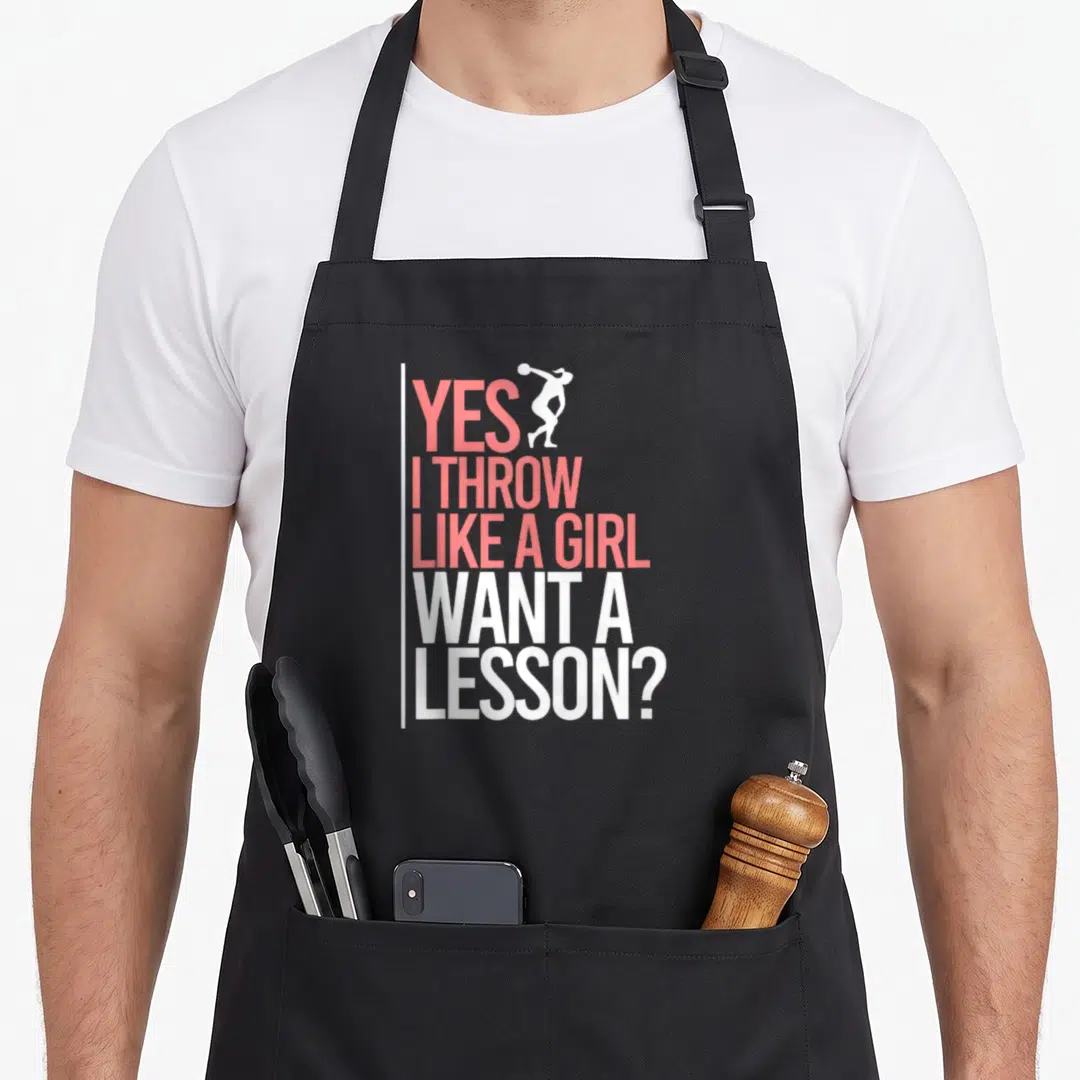 Throwing track apron - Pink and white stacked text YES I THROW LIKE A GIRL WANT A LESSON? with athlete silhouette — shown on a black cotton canvas apron against a white background