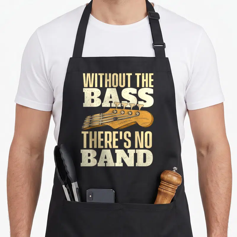 Bassist guitarist apron - Distressed text reading WITHOUT THE BASS THERE'S NO BAND above an orange-brown bass guitar — shown on a black cotton canvas apron against a white background