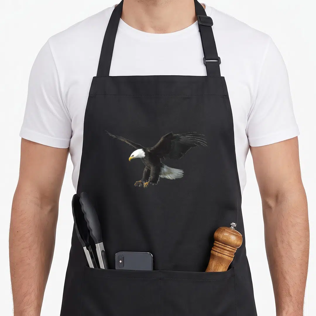 Flying eagles apron - Bald eagle in flight with brown white and yellow feathers centered on apron front — shown on a black cotton canvas apron against a white background