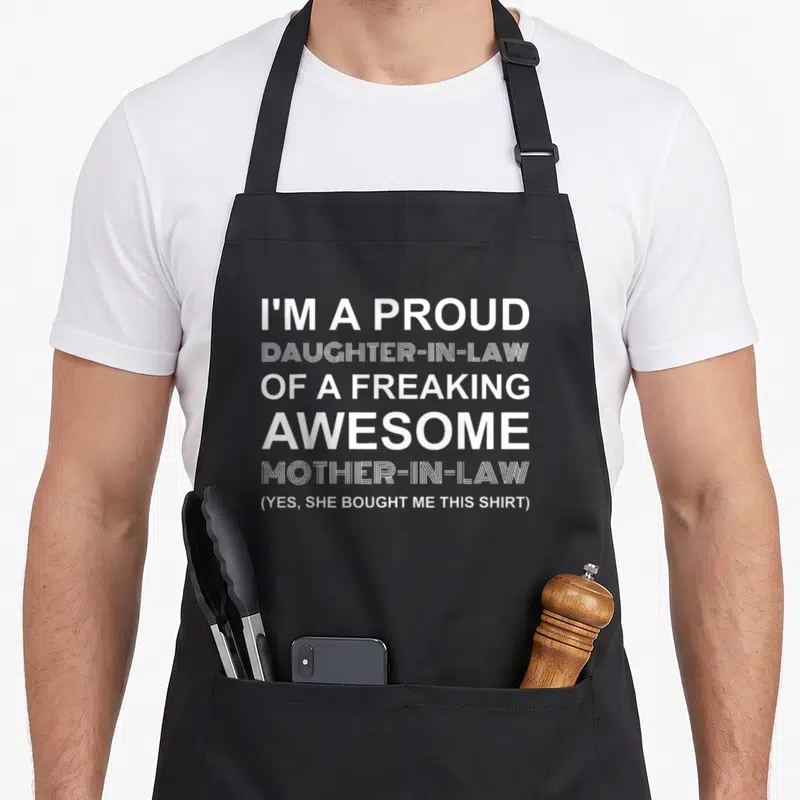 Extended mom and daughter aprons - White stacked text reading proud daughter-in-law of awesome mother-in-law bought me — shown on a black cotton canvas apron against a white background