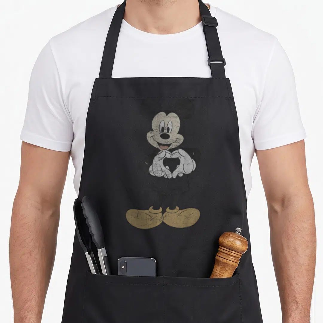 Hand friends apron - Distressed Mickey Mouse forming a heart shape with hands in black white and yellow — shown on a black cotton canvas apron against a white background