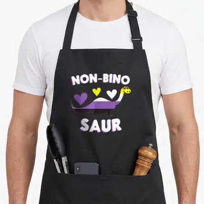 Non dinosaur apron - Dinosaur with purple white black stripes, three hearts, NON-BINO SAUR text in white with purple — shown on a black cotton canvas apron against a white background
