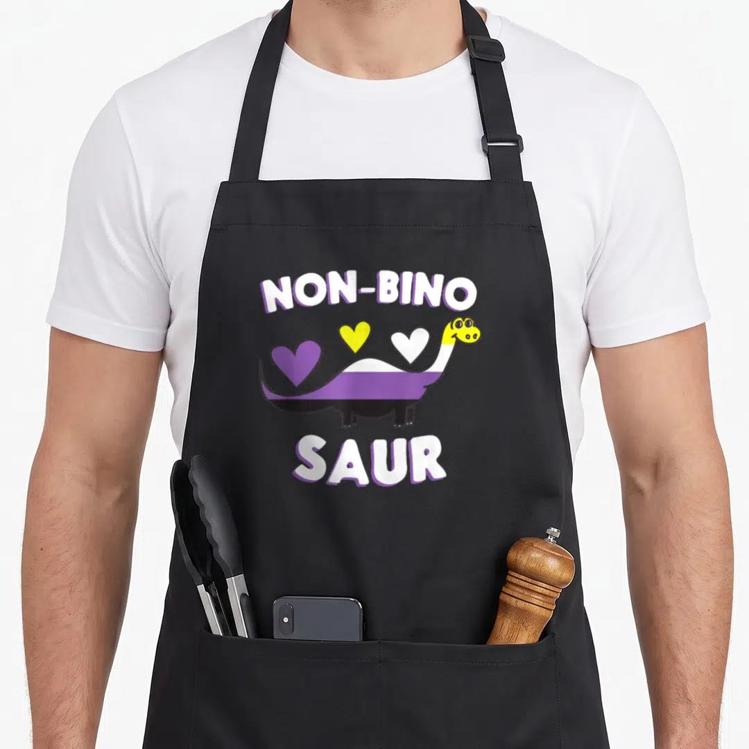 Non dinosaur apron - Dinosaur with purple white black stripes, three hearts, NON-BINO SAUR text in white with purple — shown on a black cotton canvas apron against a white background