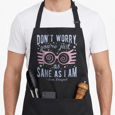 Luna a's aprons - Pink spectacles with spiral lenses surrounded by blue text and white stars — shown on a black cotton canvas apron against a white background