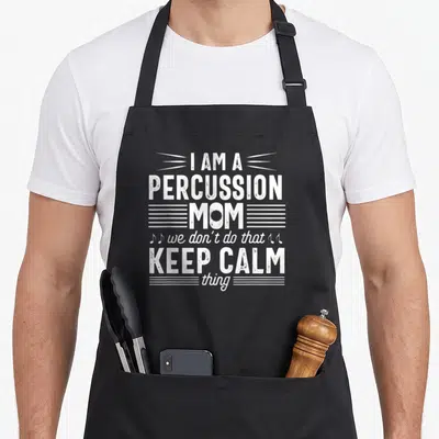 Percussion band mom apron - White stacked text reading I AM A PERCUSSION MOM with musical notes and decorative lines — shown on a black cotton canvas apron against a white background