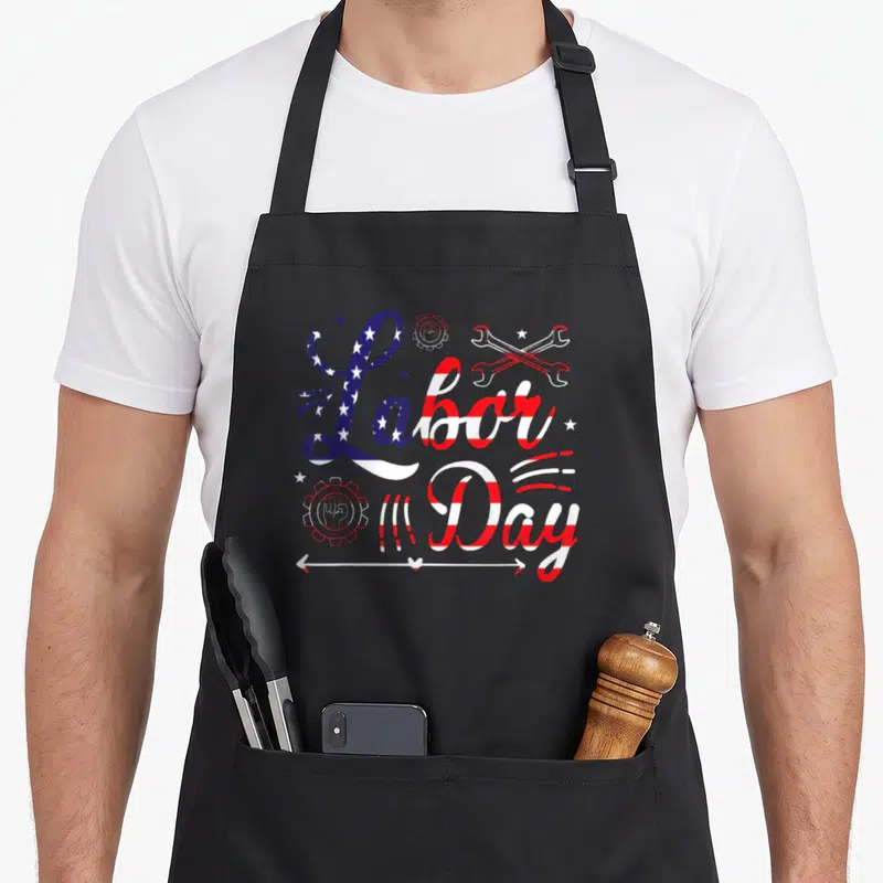 Funny labor union aprons - Labor Day text in blue white and red flag patterns with gears wrenches stars and arrow — shown on a black cotton canvas apron against a white background