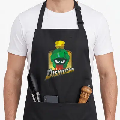 Disintegrate crazy bunny lady apron - Green helmeted alien with red suit below jagged DISINTEGRATE text on yellow — shown on a black cotton canvas apron against a white background