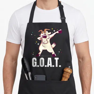 Dab goat apron - Cartoon cream goat dabbing with G.O.A.T. text and scattered stars — shown on a black cotton canvas apron against a white background