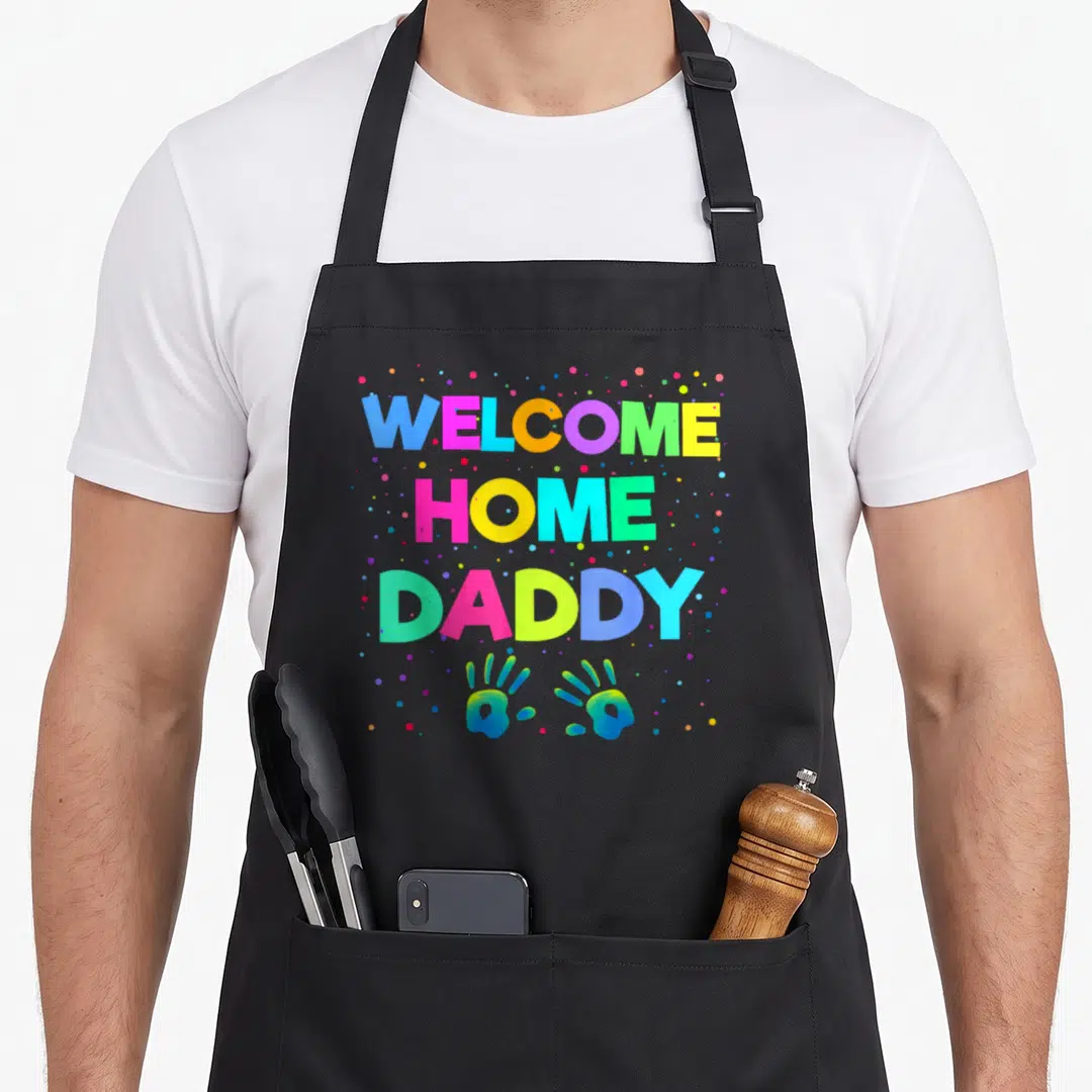 Military daddy apron - WELCOME HOME DADDY text with two handprints and colorful dots — shown on a black cotton canvas apron against a white background