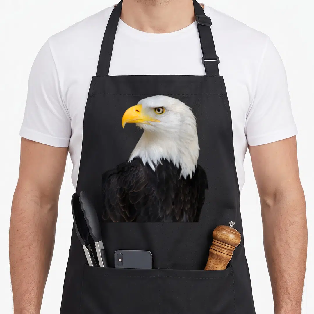 Bird eagles apron - Bald eagle profile photo with white head, brown wings, and yellow beak — shown on a black cotton canvas apron against a white background