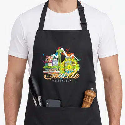 Needle seattle apron - Cartoon Seattle skyline with Space Needle, Ferris wheel, ferry, andPUBLIC MARKET text — shown on a black cotton canvas apron against a white background
