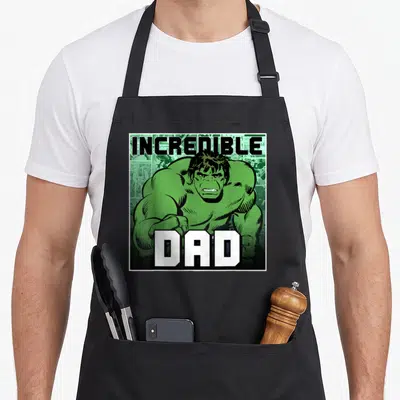 Incredible father day apron - Hulk cartoon figure with INCREDIBLE DAD text on comic panel background — shown on a black cotton canvas apron against a white background