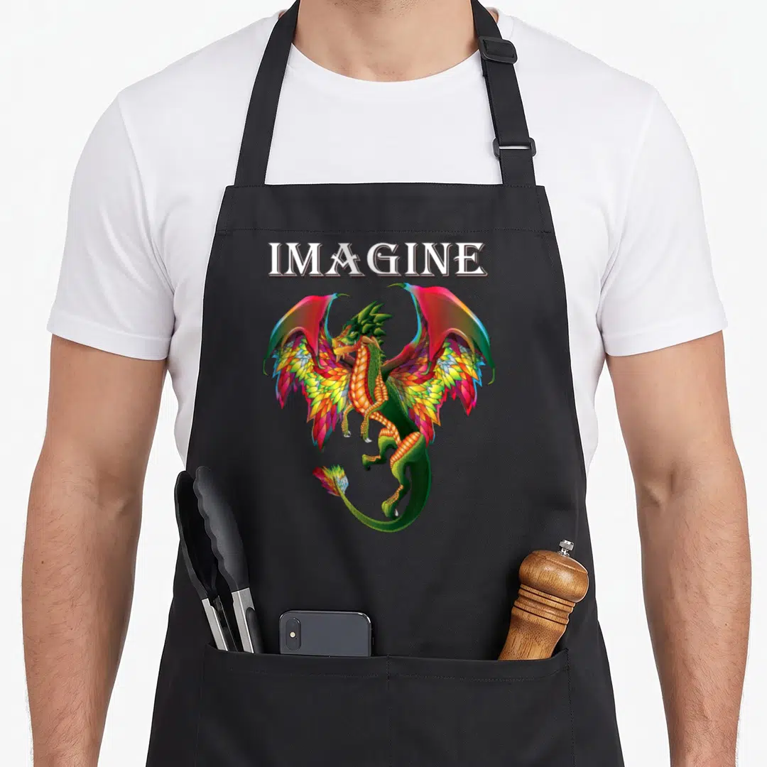 Breathing dragon apron - Colorful cartoon dragon with rainbow wings below white IMAGINE text — shown on a black cotton canvas apron against a white background