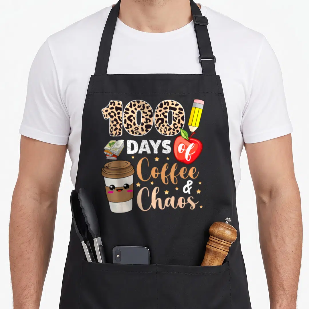 Chao 100th teacher apron - Cartoon coffee cup, books, red apple, pencil, and 100 Days of Coffee Chaos text in leopard — shown on a black cotton canvas apron against a white background