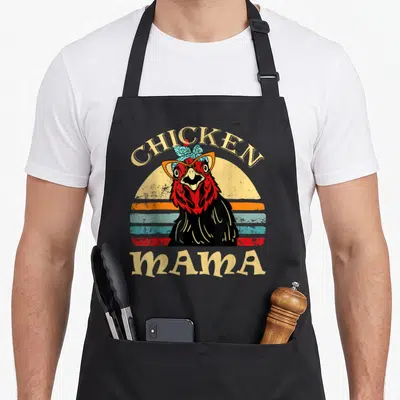Momma hen apron - Retro black chicken with glasses and bow under arched CHICKEN MAMA text — shown on a black cotton canvas apron against a white background