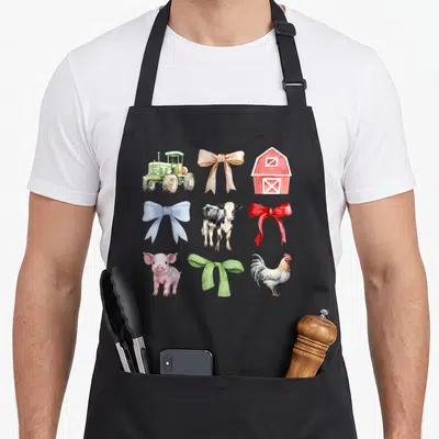 Cow chicken apron - Watercolor grid of tractor, barn, cow, pig, rooster and four colored bows — shown on a black cotton canvas apron against a white background