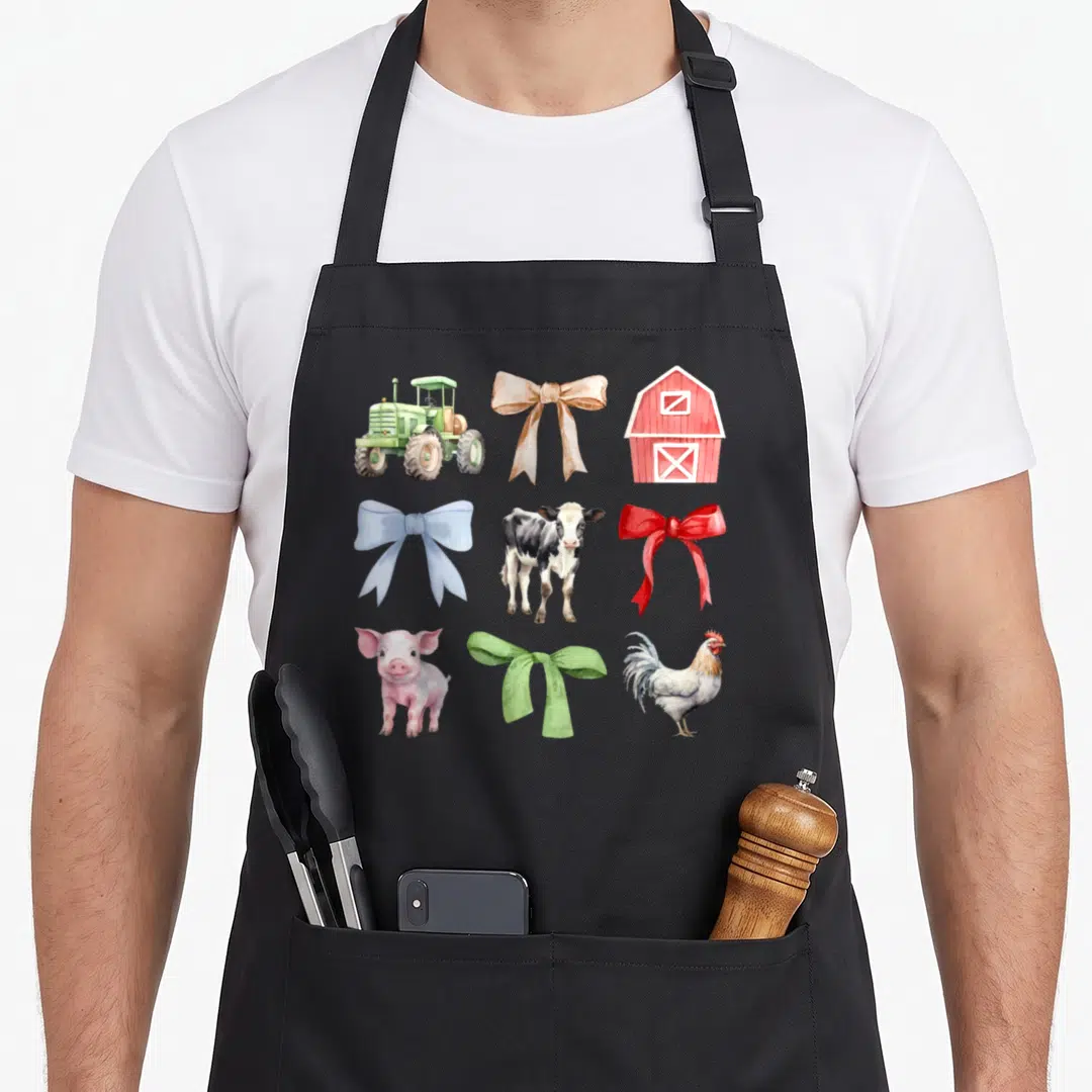 Cow chicken apron - Watercolor grid of tractor, barn, cow, pig, rooster and four colored bows — shown on a black cotton canvas apron against a white background