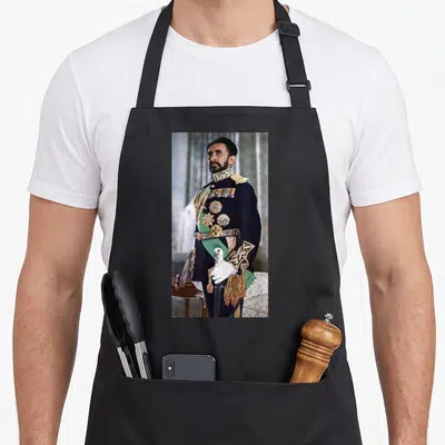 Emperor ethiopian apron - Photo of Haile Selassie in dark blue military uniform with gold medals and white gloves — shown on a black cotton canvas apron against a white background