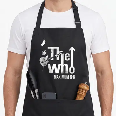 Maximum r aprons - White distressed text The Who Maximum R&B with electric guitar overlapping letters and upward arrow — shown on a black cotton canvas apron against a white background